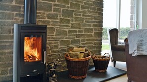 A stone wall, a fireplace with a visible fire, wicker baskets, and a chair.