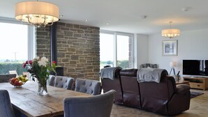 A modern living room with a stone wall, a dining area with a wooden table and chairs, leather sofas, and a TV.