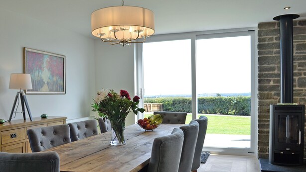 A dining area with a wooden table, grey upholstered chairs, a vase with flowers, and a chandelier.