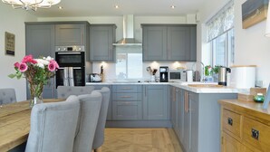 A modern kitchen with grey cabinets, a wooden dining table, and a vase of flowers.