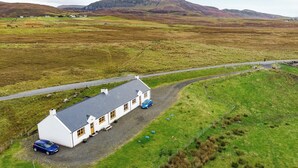 A white house with a grey roof, a gravel driveway, and a blue car parked in front. - 2 bedroom accommodation in Hungladder, near Uig (Hungladder, near Uig)