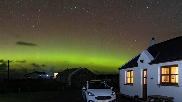A white building with a car parked in front, under a night sky with visible stars and green aurora. - 2 bedroom accommodation in Hungladder, near Uig (Hungladder, near Uig)