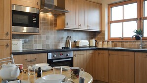 A modern kitchen with wooden cabinets, stainless steel appliances, and a dining area with a round table set for two. - 2 bedroom accommodation in Hungladder, near Uig (Hungladder, near Uig)