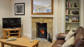 A living room with a stone fireplace, a television, a bookshelf, and a leather sofa.