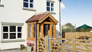 A white house with a wooden gate and a small wooden structure with a tiled roof.