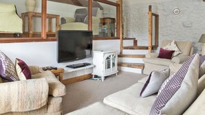 A cozy living room with a television, sofa, and a stone wall. - Lavender Cottage - UK4061 (Buxton)