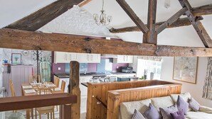 A rustic kitchen with wooden beams, a dining area with a table and chairs, and a living room with a sofa and cushions. - Lavender Cottage - UK4061 (Buxton)