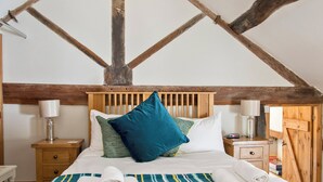 A bedroom with a wooden ceiling, a bed with striped bedding, two bedside tables with lamps, and a wooden wardrobe. - Lavender Cottage - UK4061 (Buxton)