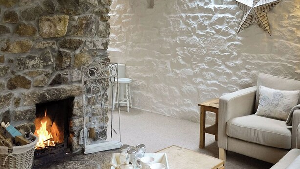 A cozy living room with a stone fireplace, a wooden coffee table, and a comfortable sofa. - 2 bedroom accommodation in Godolphin Cross, Helston (Godolphin Cross, Helston)