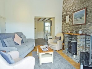 A living room with a sofa, armchair, coffee table, fireplace, and stone wall. - 2 bedroom accommodation in Three Crosses, Gower, Swansea (Three Crosses, Gower, Swansea)