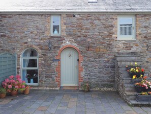 A stone building with a green door, a window with a sign reading 'The Granary,' and flower planters on the steps. - 2 bedroom accommodation in Three Crosses, Gower, Swansea (Three Crosses, Gower, Swansea)