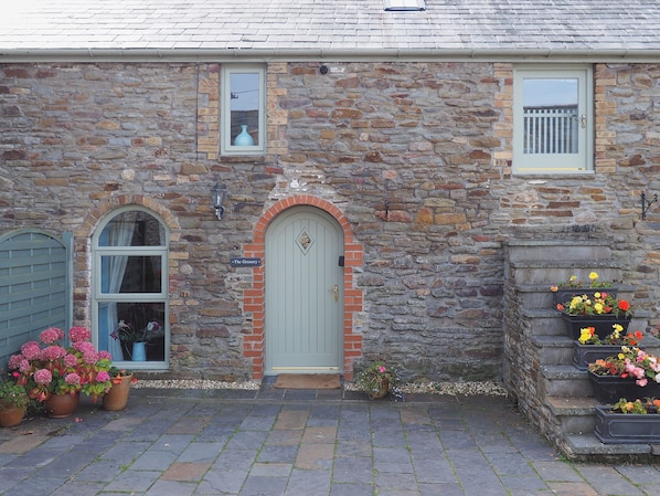 Un edificio de piedra con una puerta verde, una ventana con un cartel que dice 'The Granary', y macetas con flores en los escalones.