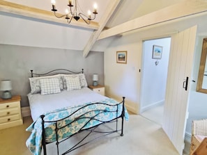 Un dormitorio con cama, mesitas de noche, candelabro, puerta y un cuadro en la pared.