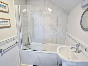 Un baño con ducha de vidrio, lavamanos blanco y pared de mármol.