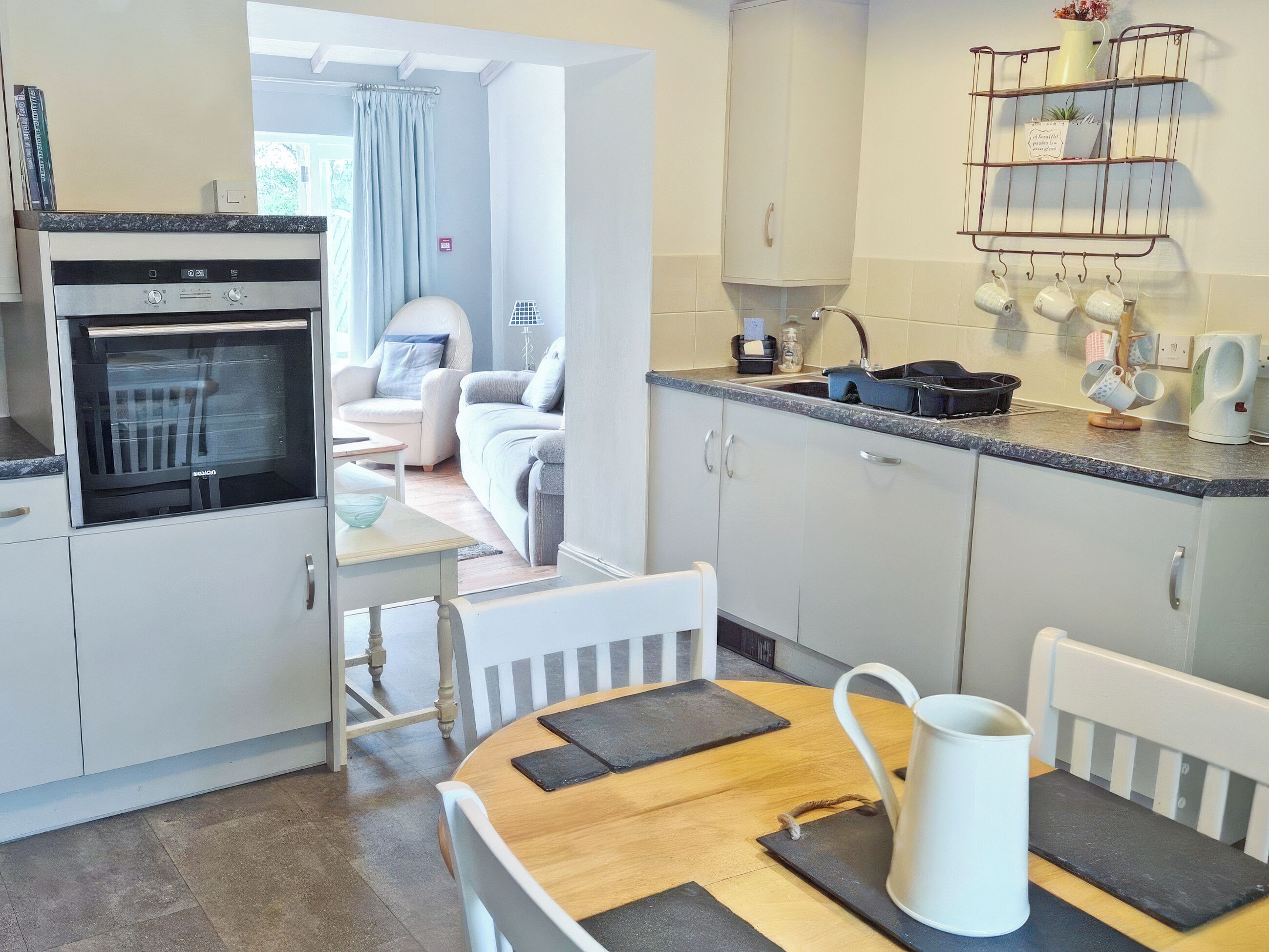 A modern kitchen with a built-in oven, a dining table with chairs, and a view into the living area.