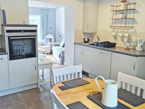 A modern kitchen with a built-in oven, a dining table with chairs, and a view into the living area. - 2 bedroom accommodation in Three Crosses, Gower, Swansea (Three Crosses, Gower, Swansea)