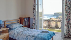 A bedroom with a bed, a bedside table, a bookshelf, and a view of the ocean through a balcony. - 2 bedroom accommodation in Saltburn-by-the-Sea (Saltburn-by-the-Sea)