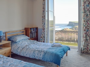 Une chambre à coucher comprenant un lit, une table de chevet, une bibliothèque et une vue sur l’océan depuis un balcon.