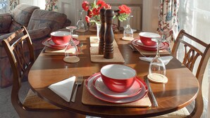 A dining table set for four with red and white plates, glasses, and a vase with red flowers. - 2 bedroom accommodation in Saltburn-by-the-Sea (Saltburn-by-the-Sea)