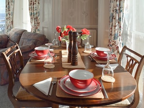 Una mesa de comedor con platos, tazones y cubiertos rojos, rodeada de sillas de madera.