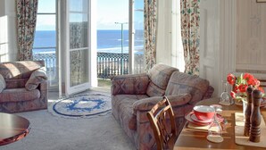 A room with a sofa, a dining table set with red and white plates, and a view of the sea through large windows. - 2 bedroom accommodation in Saltburn-by-the-Sea (Saltburn-by-the-Sea)