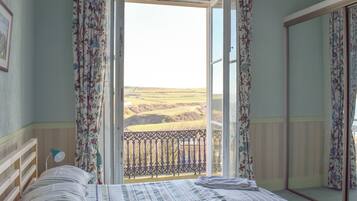 A bedroom with a bed, a bedside lamp, a mirror, and a view of the countryside through an open door.