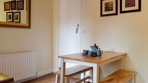 Una habitación con un radiador blanco, una mesa de madera con una tetera azul y varias obras de arte enmarcadas en la pared.