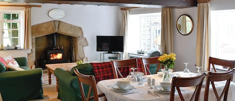 A cozy living room with a fireplace, a dining area with a table set for four, and a television in the corner.