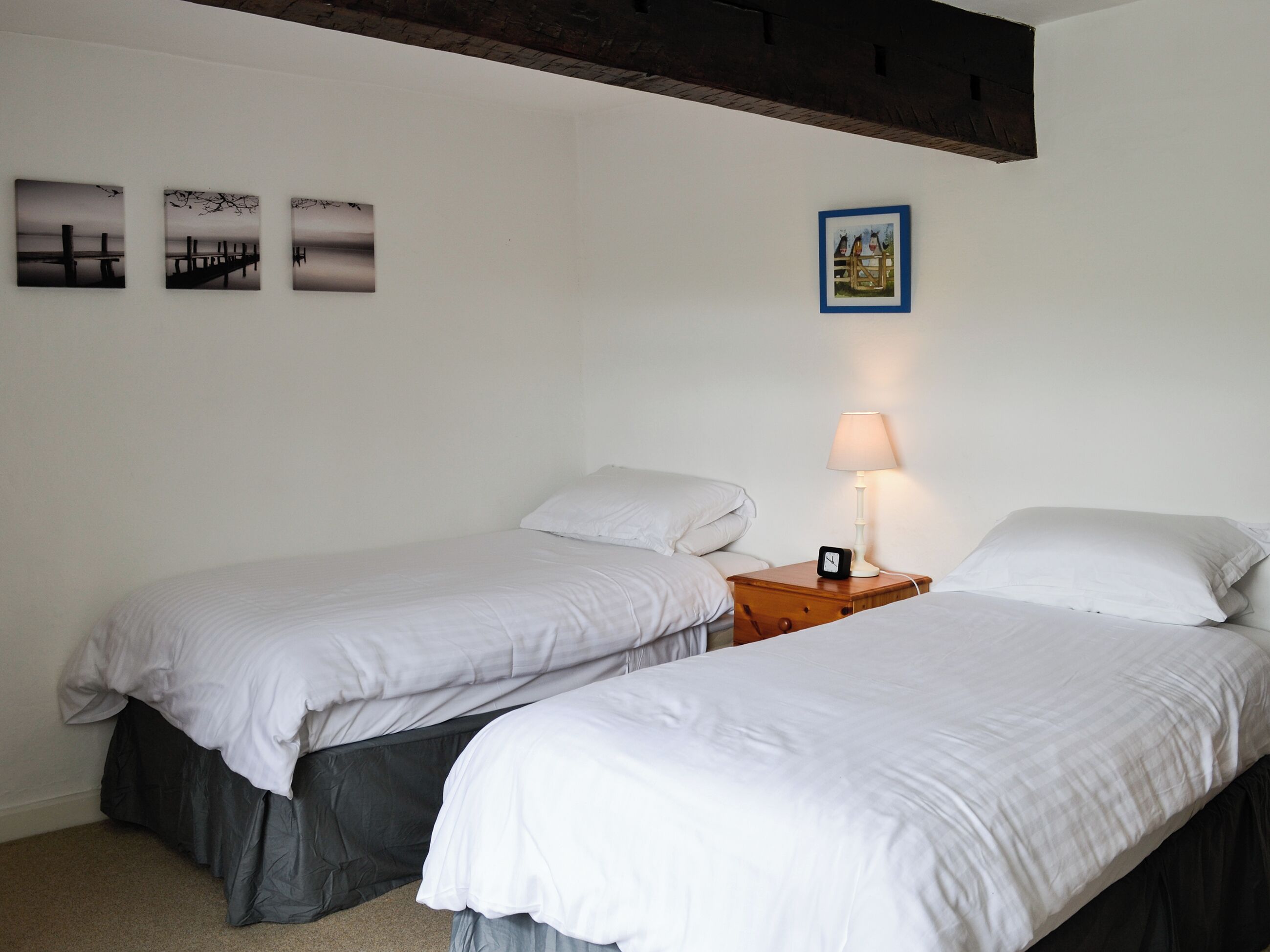 A room with two single beds, a nightstand with a lamp, and three framed pictures on the wall.