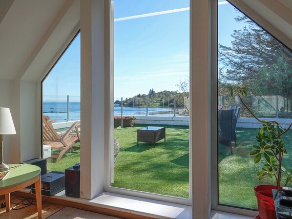 A room with large windows, a view of the sea, a lawn, and outdoor furniture.