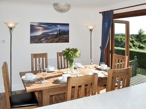 A dining area with a wooden table set for four, two chairs, a vase with flowers, and two floor lamps.