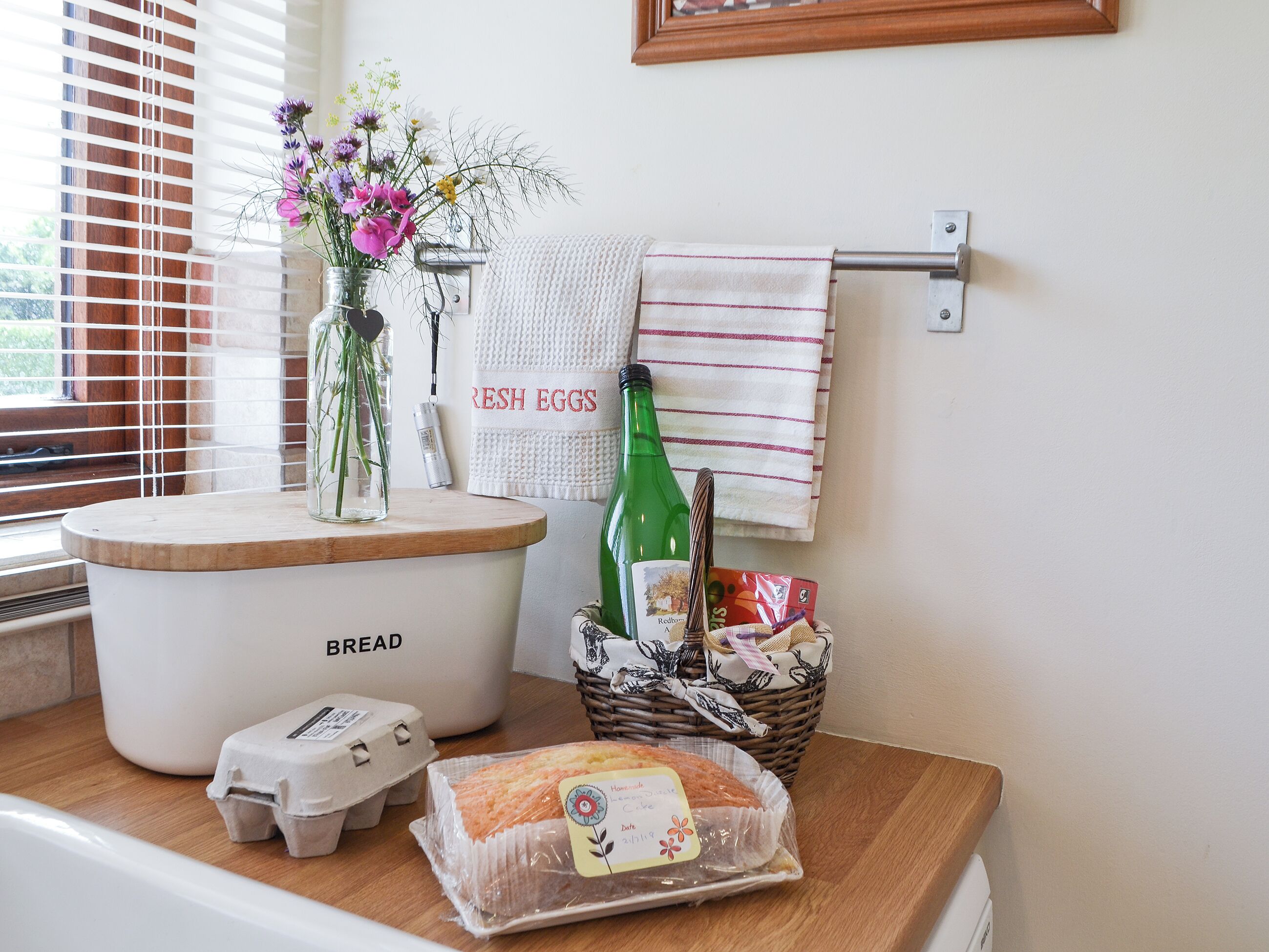 A kitchen counter with a bread maker, eggs, a bottle of olive oil, a basket of bread, and a loaf of bread.