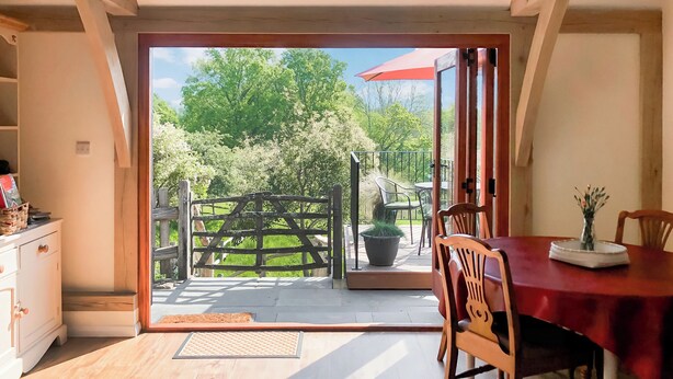 Un coin repas avec une table et des chaises en bois, une nappe rouge et une vue sur un jardin, visible à travers une porte vitrée.