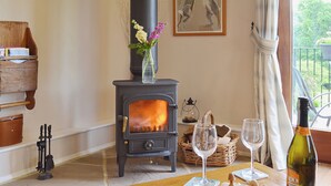 Un salon chaleureux avec un poêle à bois, une table en bois sur laquelle se trouvent des verres et une bouteille, et un vase rempli de fleurs accroché au mur.