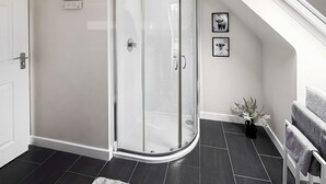 Un baño moderno con cabina de ducha de vidrio, una puerta blanca y una pequeña planta.