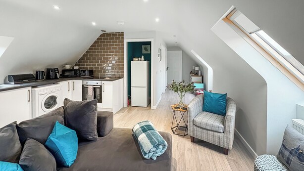 Un espacio habitable compacto con kitchenette, un sofá, una silla y una pequeña mesa.