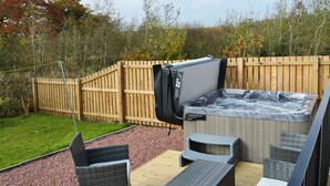 Un jacuzzi con muelle de madera, mobiliario de mimbre y cerca de madera en un patio trasero.