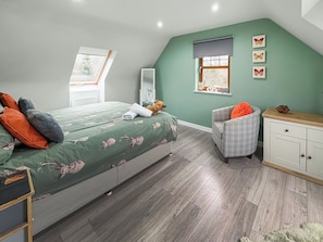 Een slaapkamer met een bed, een stoel, een dressoir en een raam met uitzicht op bomen.