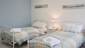 A bedroom with two beds, a nightstand, a lamp, and two wall-mounted pictures.