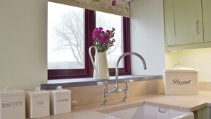 A kitchen with a window, a sink, and storage containers labeled 'BISCUITS,' 'TEA,' and 'COFFEE.'