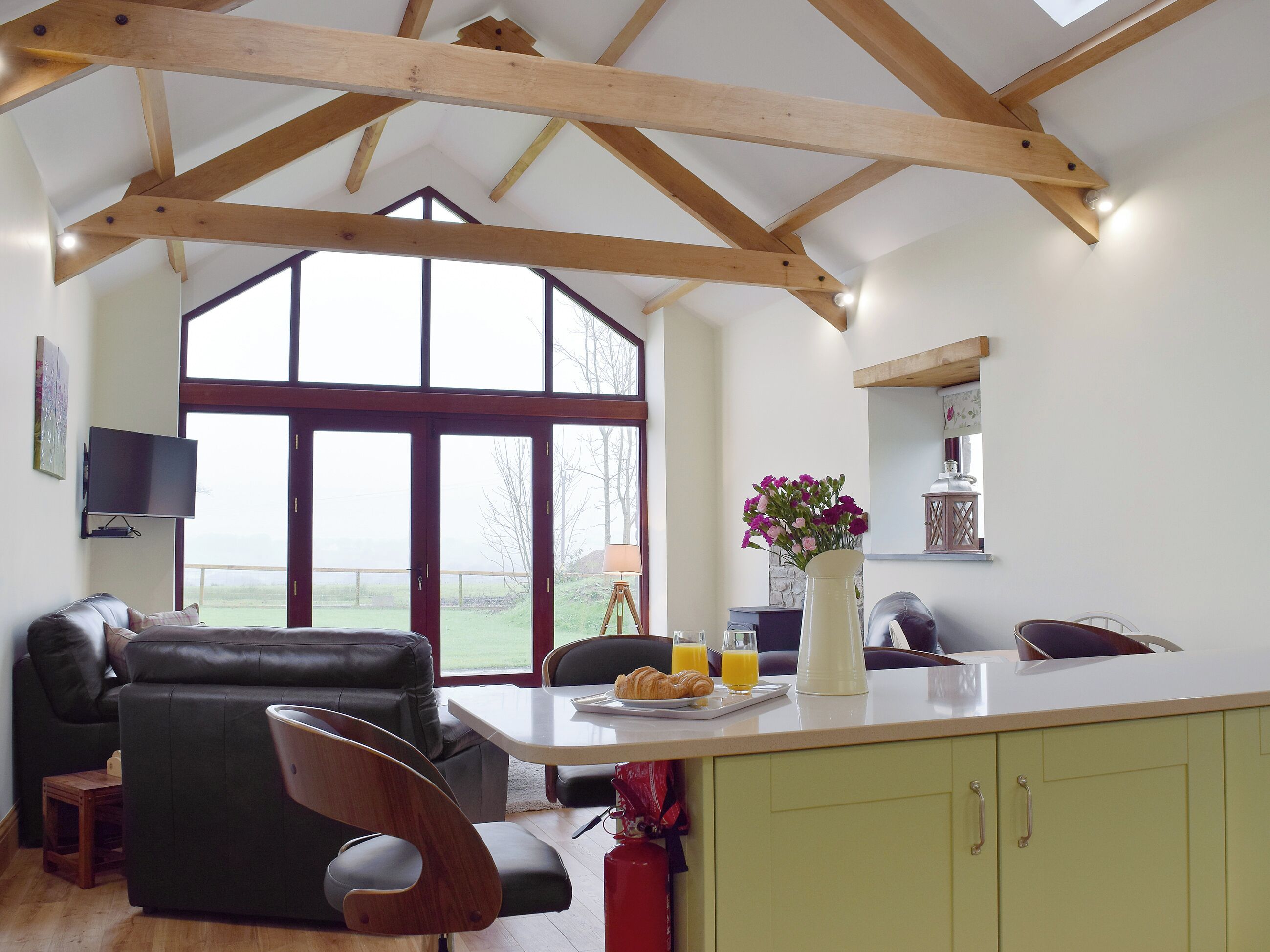 A spacious living area with a high ceiling, a large window, a dining table with breakfast items, and a cozy seating arrangement.