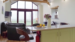 A spacious living area with a high ceiling, a large window, a dining table with breakfast items, and a cozy seating arrangement.