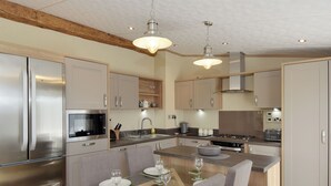 A modern kitchen with stainless steel appliances, a glass dining table, and wooden flooring.