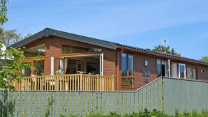 A wooden cabin with a deck, large windows, and a metal roof.