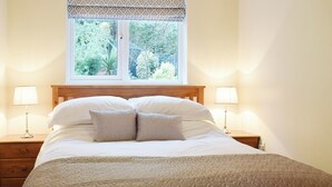 Una cama bien hecha con un edredón estampado, dos lámparas de noche y una ventana con vistas a zonas verdes.