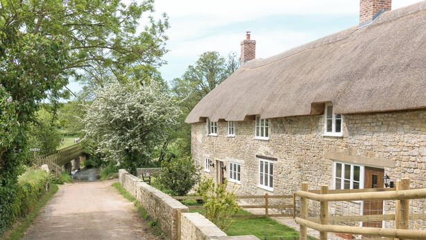 A stone cottage with a thatched roof, a stone pathway, and a wooden fence. - The Farmhouse at Higher Westwater (Axminster)