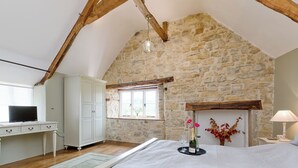 A bedroom with a stone wall, a wooden ceiling, a bed, a desk, a wardrobe, and a window with a view. - The Farmhouse at Higher Westwater (Axminster)