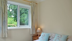 Ein Schlafzimmer mit einem Bett, zwei Kissen, einem Nachttisch, einer Lampe und einem Fenster mit Vorhängen.