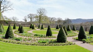 Ein formeller Garten mit ordentlich geschnittenem Formschnitt, einer Steinmauer und einem Weg.