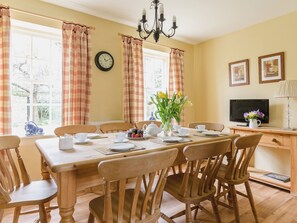 A dining room with a wooden table, chairs, a clock, a vase with flowers, a television, and framed pictures on the wall. - 4 bedroom accommodation in Pickering (Pickering)
